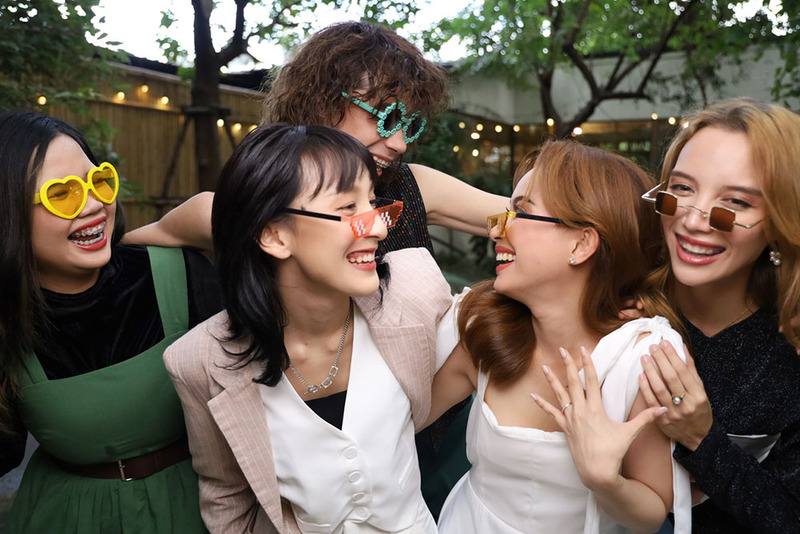 Two brides pose with their friend officiant and guests on the wedding day, outdoors
