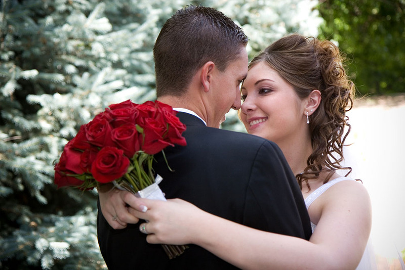 Bride and groom pose on wedding day outdoors, bride holds red roses