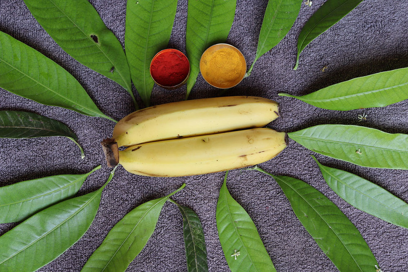 Banana tree leaves and yellow bananas are placed with dishes of sindoor powder and tumeric