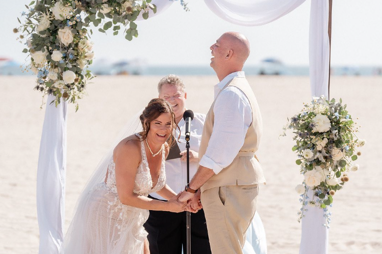 Wedding officiant Bethel Nathan performs a beach wedding in California as bride and groom laugh happily