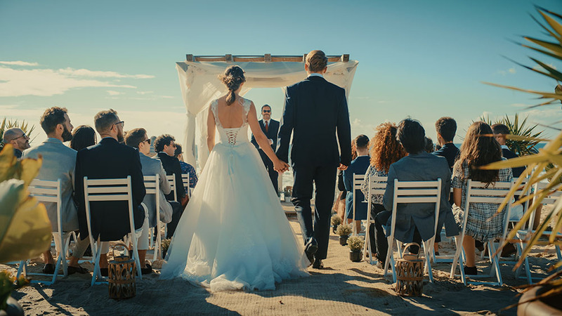 La novia y el novio caminan juntos por el pasillo durante la procesión nupcial, mientras amigos, familiares y el oficiante observan sonriendo.