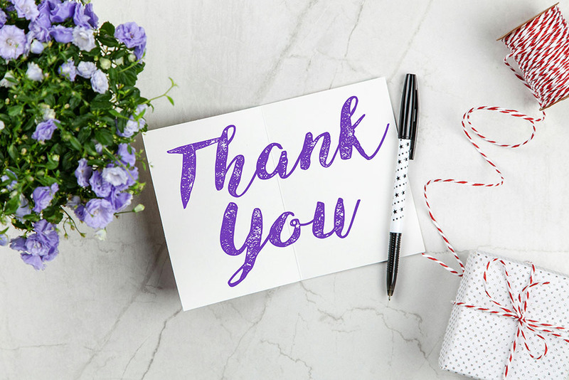 A thank you card resting on a table with purple flowers