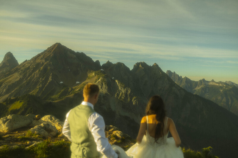 Bride and groom pose against majestic mountain peaks during an adventure wedding