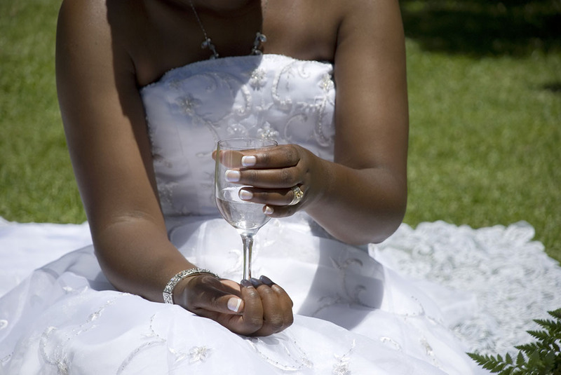 Primer plano de una novia sentada en el césped sosteniendo un vaso de agua.