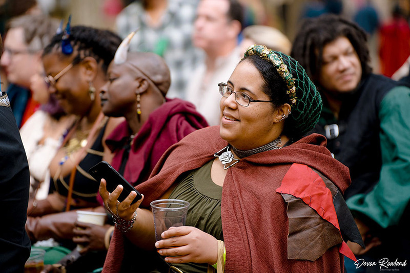 Wedding guests at ren faire wedding, looking happy during ceremony and holding phones to snap photos