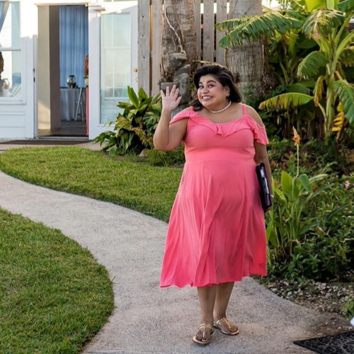 Wedding officiant Renee Reyes smiles and waves a the camera in a bright pink dress