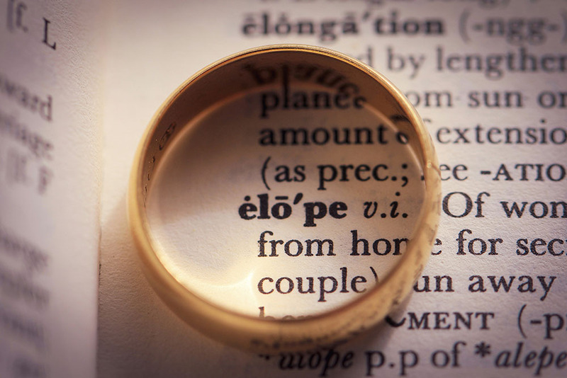 Wedding ring set on a dictionary page, circling the word 'elope' as a symbol of eloping