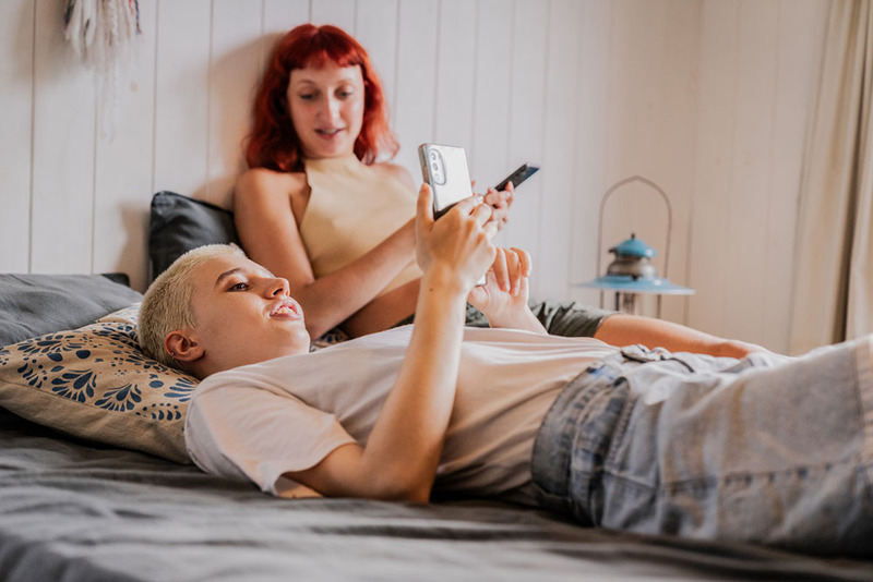 Young engaged couple uses AI therapy apps on their phones in bed