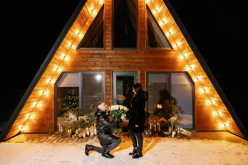 Man on one knee proposes to woman by candlelight in the snow