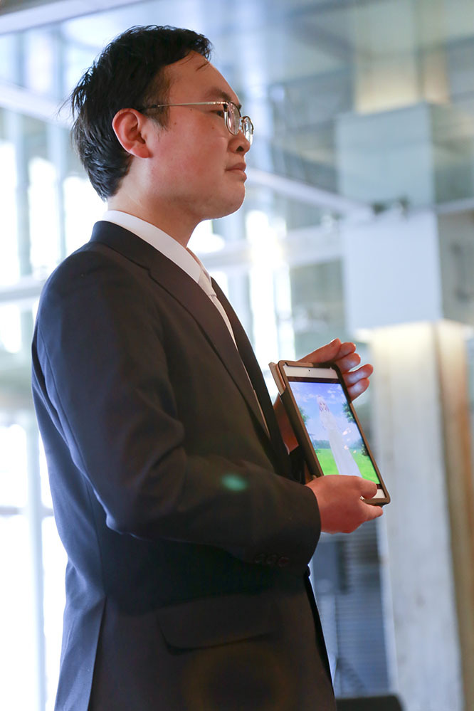 a young man poses with a tablet displaying his fictional other during a symbolic ceremony