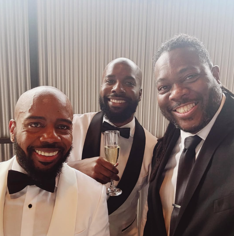 Officiant Chris poses with the happy grooms at Hangar 21