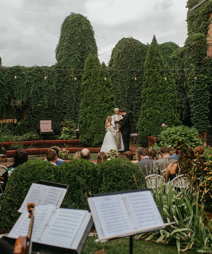 Bride and groom exchange vows with live music, beautiful green bushes