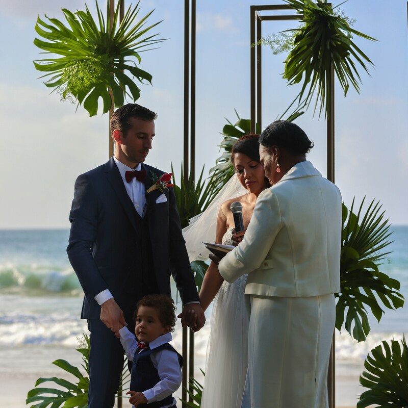A bride and groom stand with their friend officiant and young child on the wedding day
