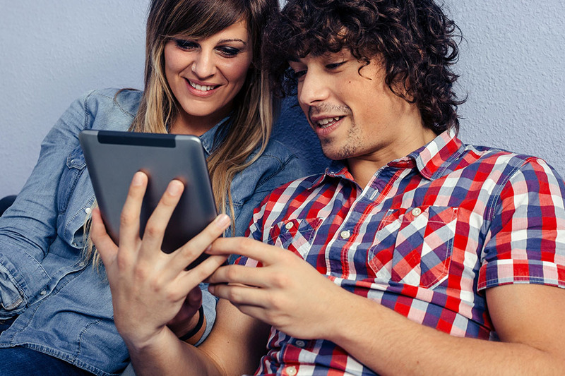 Un hombre y una mujer jóvenes se sientan en un sofá leyendo reseñas de iglesias en línea para encontrar el mejor lugar para ser ordenado en línea en una tableta.