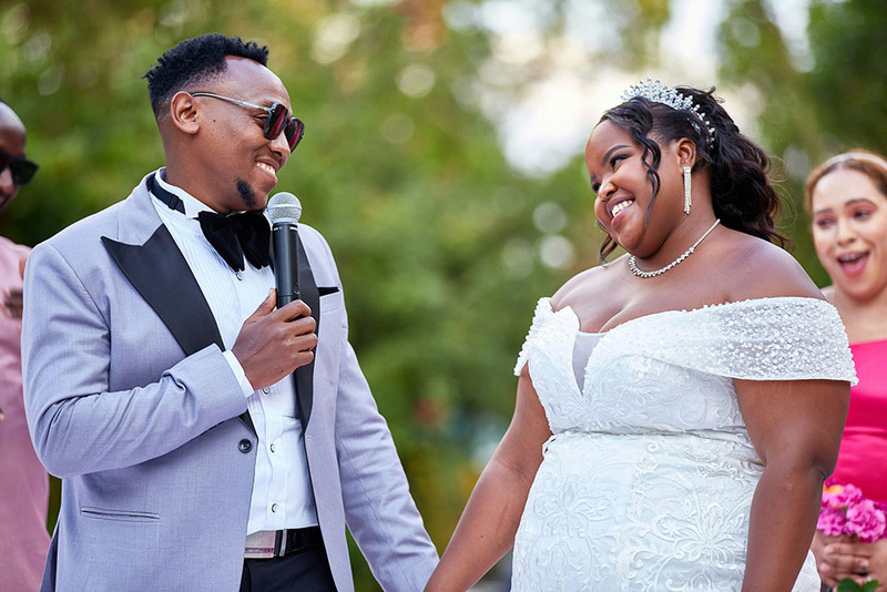 bride says his vows to smiling bride, holding microphone