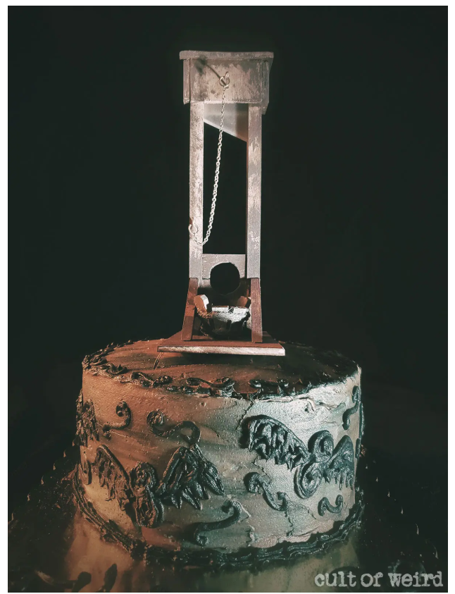 Close up of a gothic dark green cake with a custom guillotine cake topper design