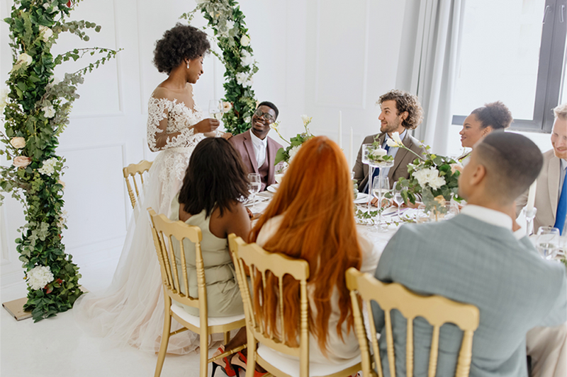 Bride gives toast at brunch wedding reception, with groom and guests
