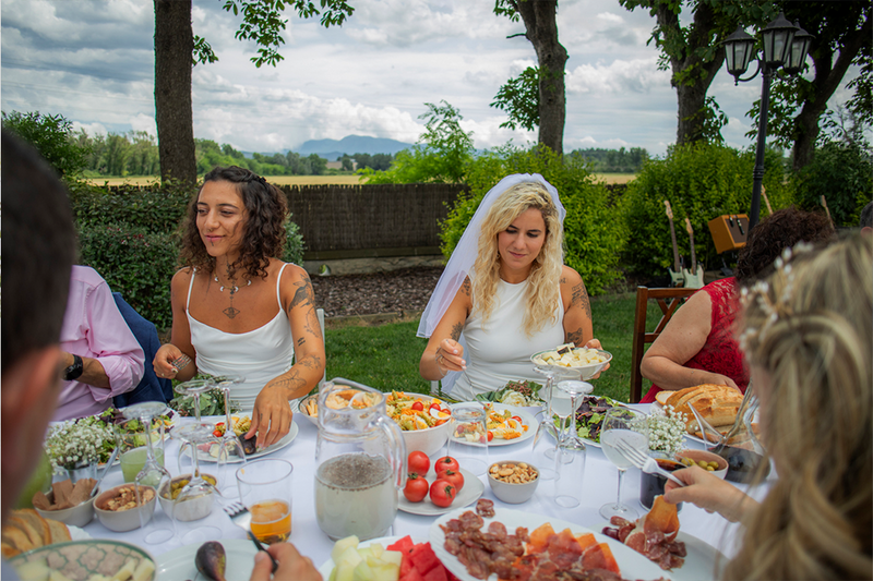 brides join guests at the table for a wedding brunch outdoors in nature