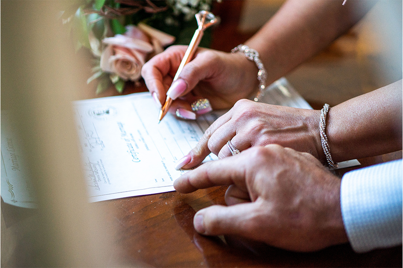 Close up of the wedding officiant helping a witness sign the marriage license