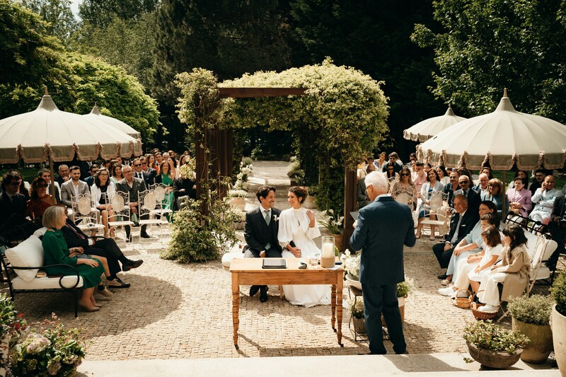 Bride and groom seated at the wedding altar with guests in background, outdoor garden wedding venue