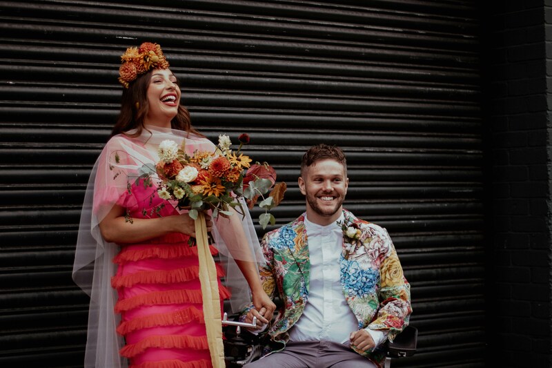 bride and groom in colorful wedding attire, groom is seated in wheelchair