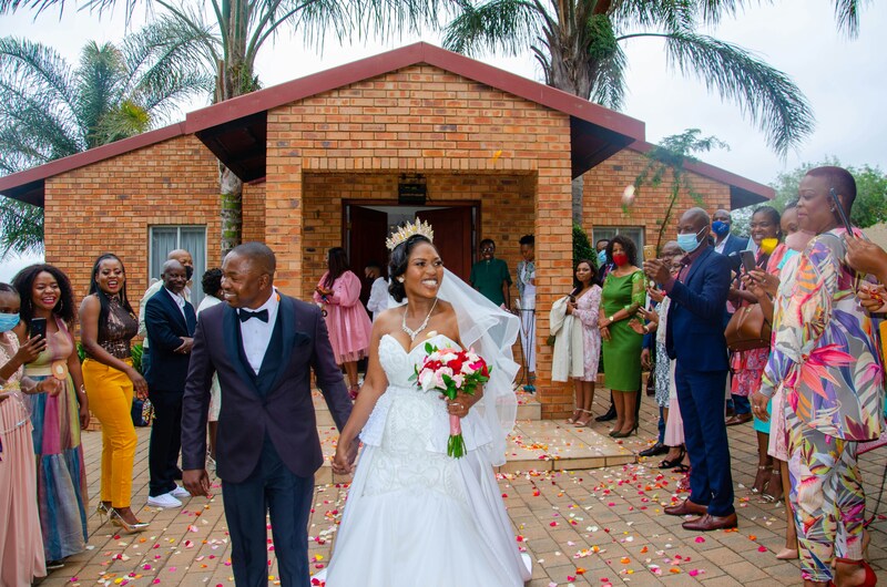 bride and groom leave wedding venue with guests and family watching happily