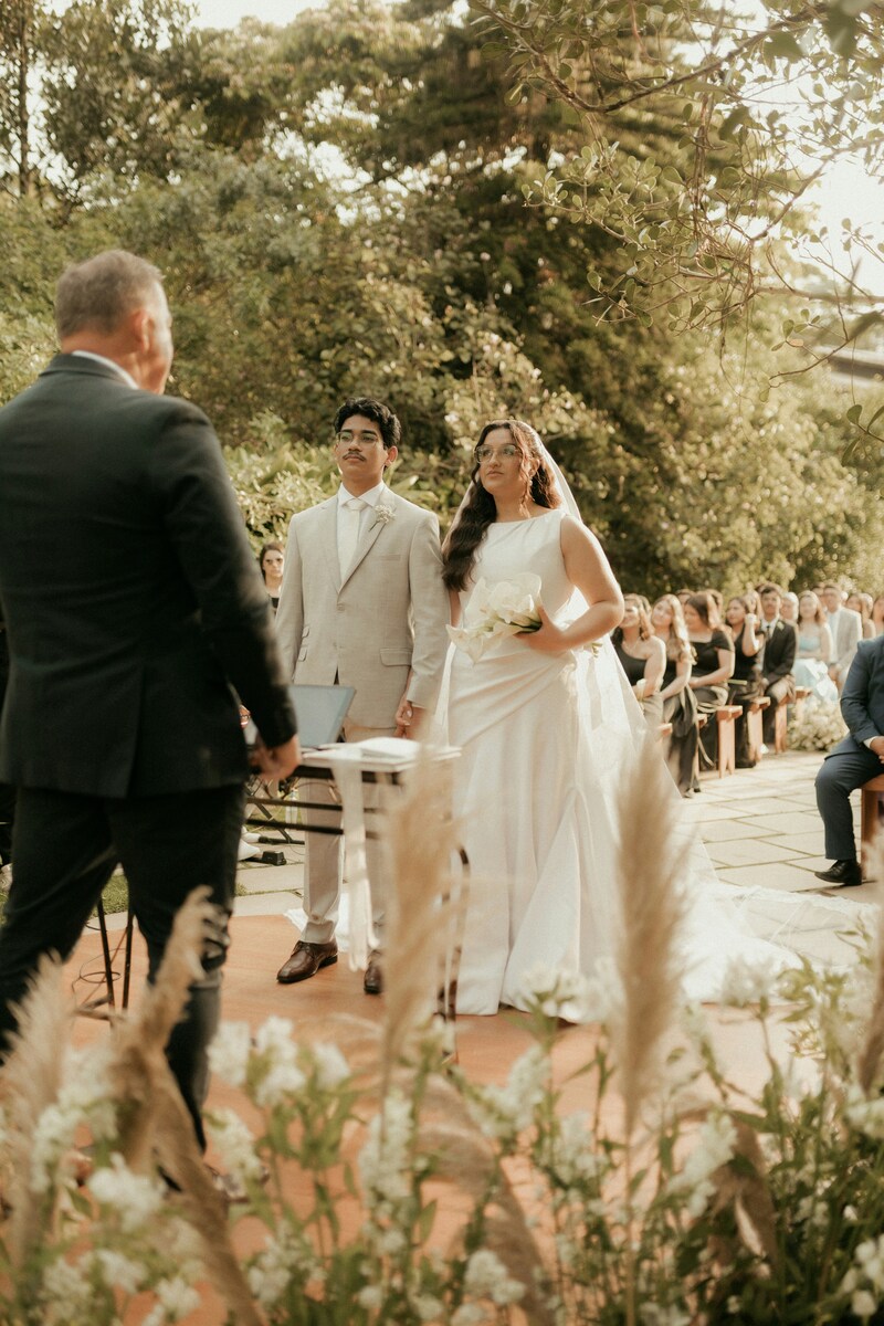 Un oficiante de bodas celebra la ceremonia nupcial al aire libre para los novios, mientras la familia observa con alegría.