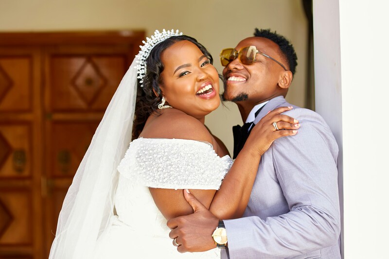Happy bride and groom in formal wedding attire embrace and pose for wedding photos, laughing happily