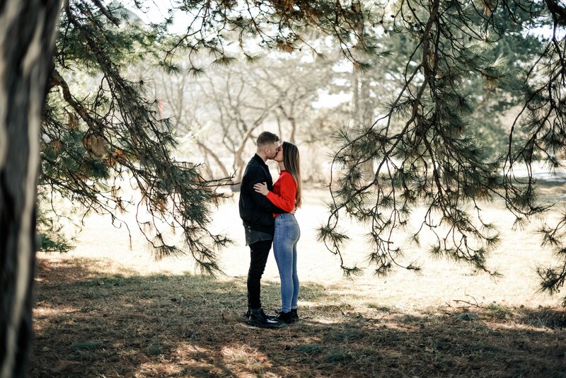 A young couple kisses, standing in a small group of trees