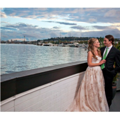 image is a photograph of Emily and Aaron O'Neill on their wedding day, standing in dress and suit in front of a beautiful view of the Lake Union waterfront in Seattle, WA