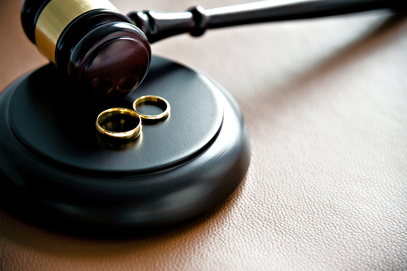 image of a darkly colored wooden gavel with a gold stripe laying on its side, next to two gold wedding rings, to imply ruling on current marriage laws