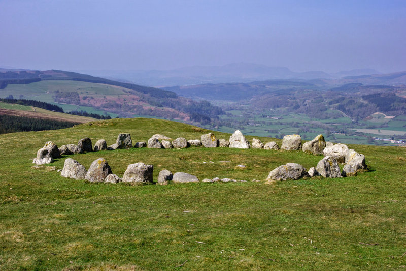 An ancient Druid stone circle in a wide green field with a blue sky behind