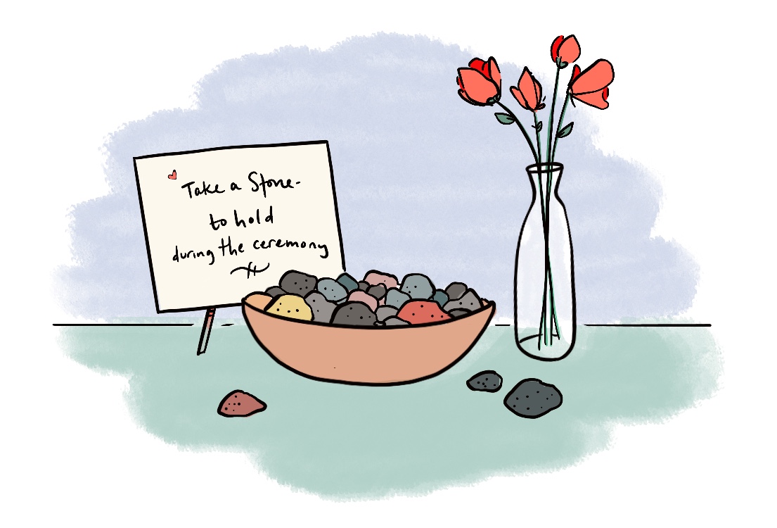 Illustration of a wedding table with a bowl of small colorful stones, ready for guests to take in order to participate in a wedding ritual stone blessing ceremony. Beside the bowl of stones is a small handwritten sign that says 'Take a stone to hold during the ceremony,' and there is a small vase with pink flowers beside it