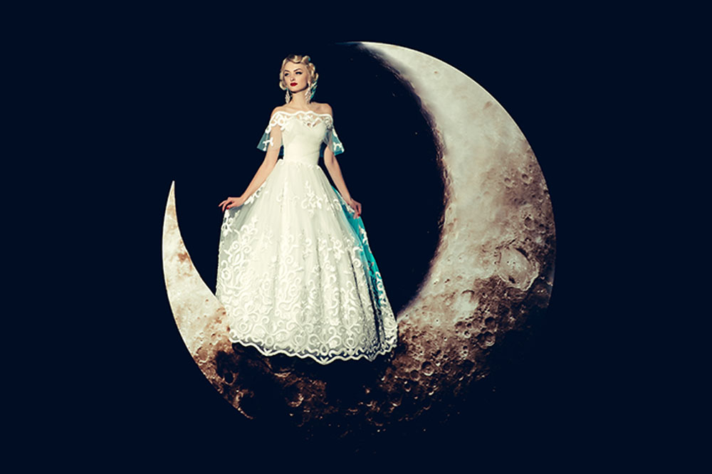 bride stands on a crescent moon in a stylized photo shoot