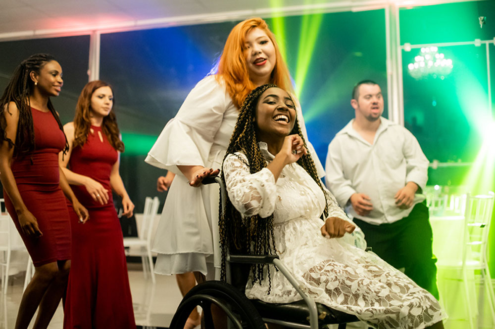 Young newlyweds on the dance floor with friends at the wedding reception, one bride is in a wheelchair
