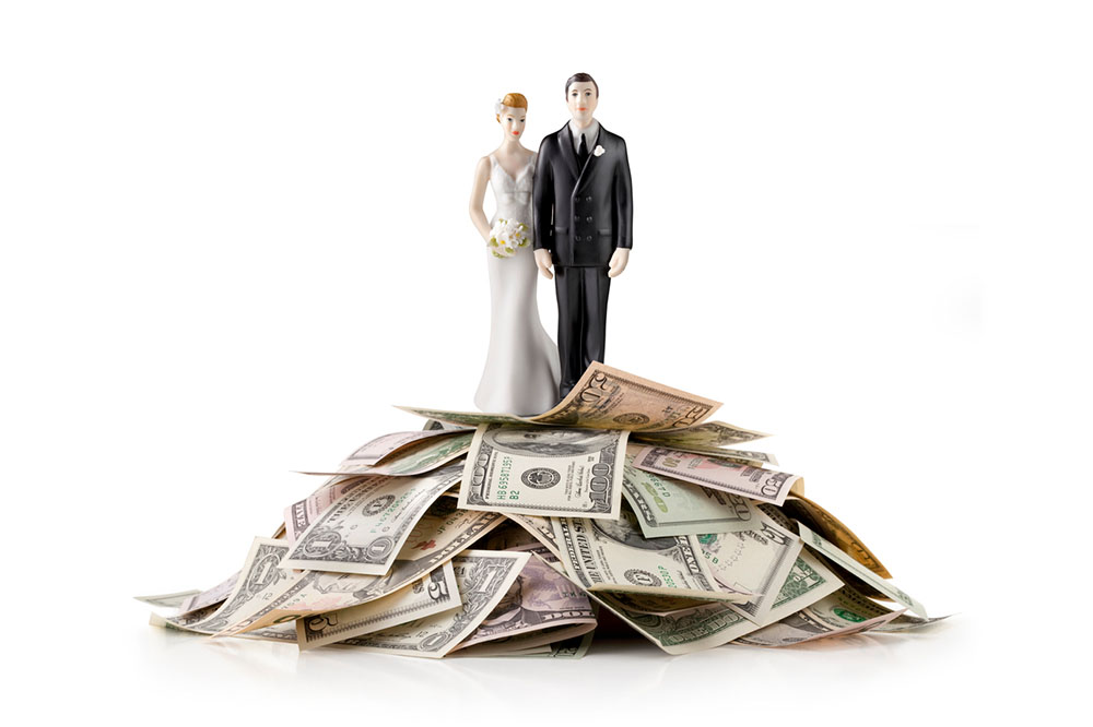 Bride and groom wedding cake topper sitting on top of a pile of money to symbolize saving money on a wedding