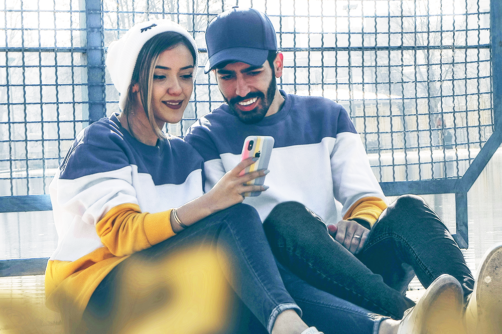 Young couple look at a phone together smiling outdoors