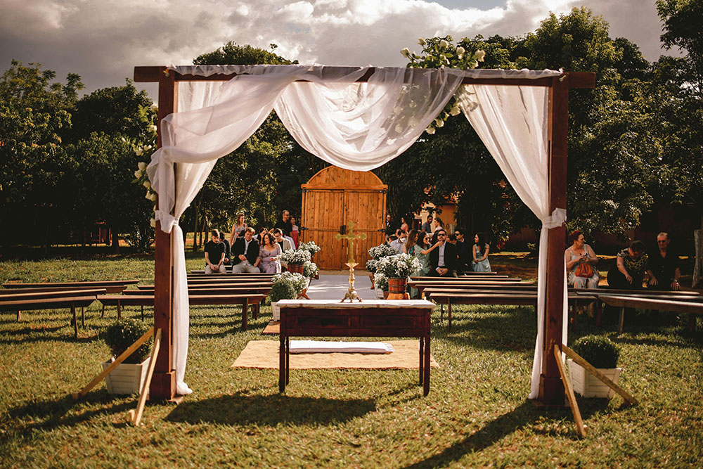 Invitadas sentadas en una boda, esperando, arco de boda arreglado con flores.