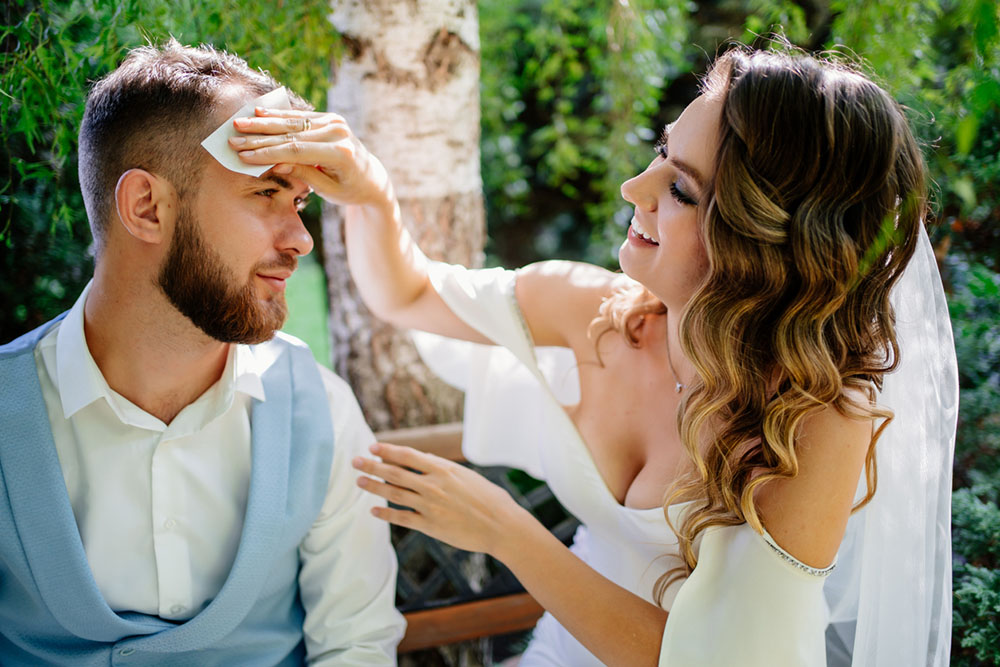 Bride smiles and wipes sweat off groom's forehead with napkin