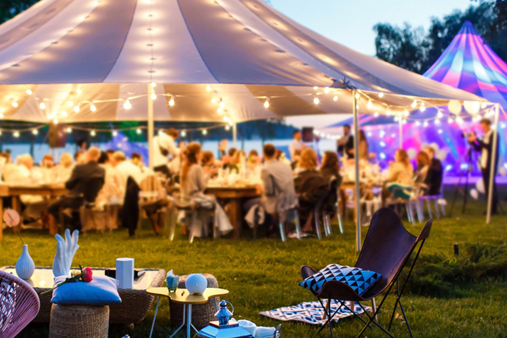 Wedding tent with colorful lights, guests gathered happily at evening