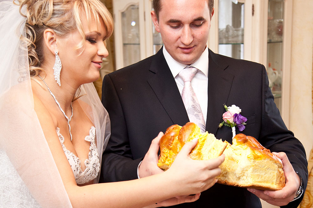 bride and groom smile and laugh as they break a traditional loaf of bread together 