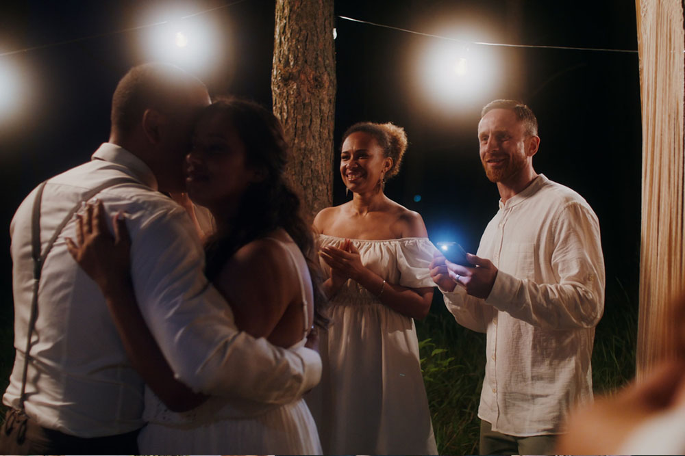 friends clap and smile as two newlyweds hug during reception dinner