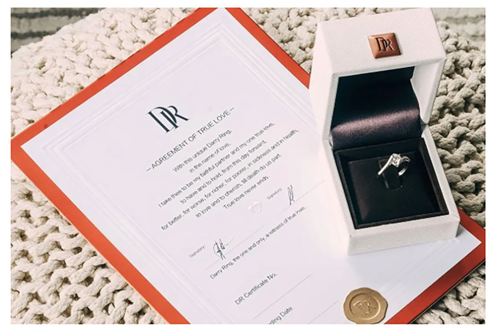 Photo shows a Darry Ring agreement next to a ring box and ring, promotional image from the company