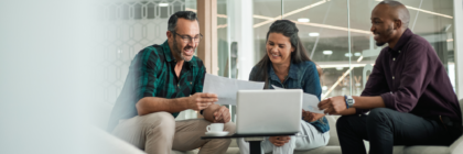 Three coworkers sitting together looking at paperwork and laughing
