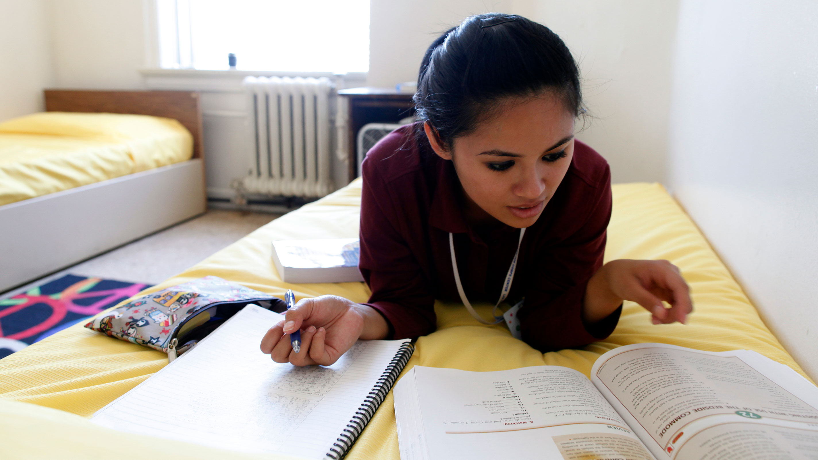 Young woman lies on dorm bed studying from a text book