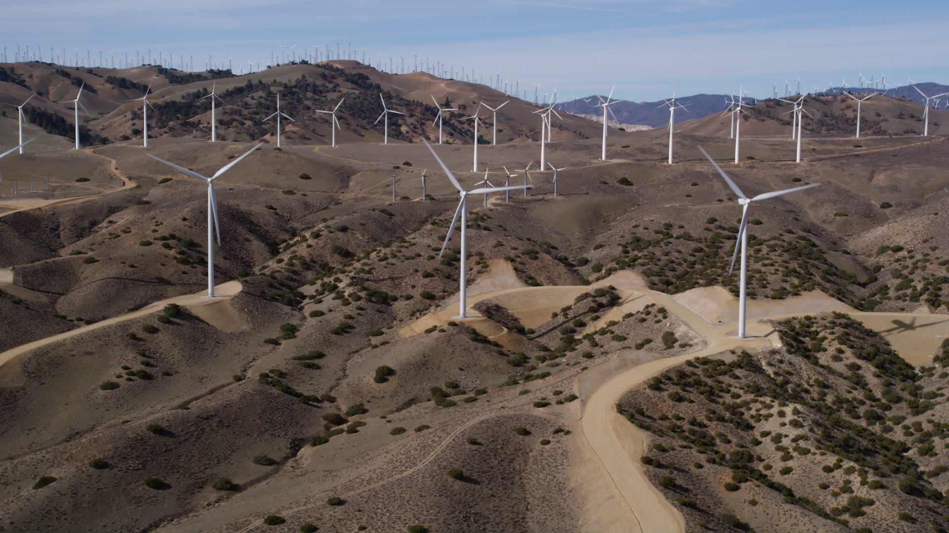 5K stock footage aerial video approaching a pair of windmills at a wind energy farm in the