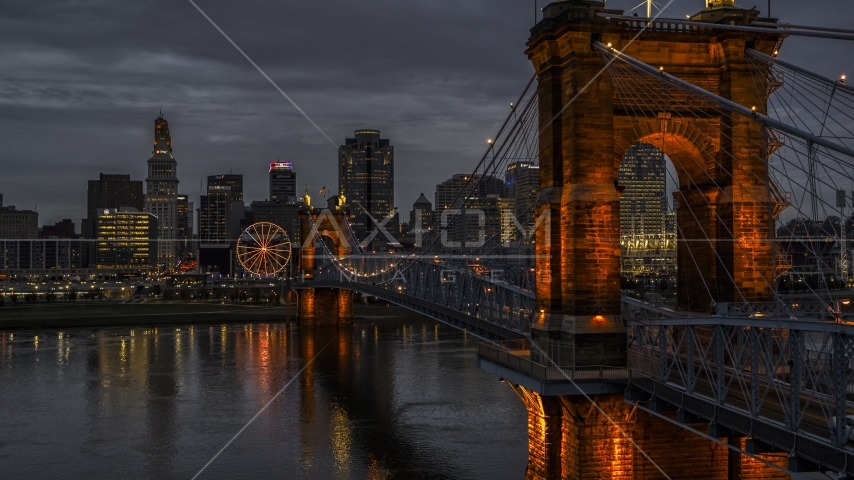 The city skyline behind Roebling Bridge lit up at twilight, seen from Ohio River, Downtown Cincinnati, Ohio Aerial Stock Photos DXP001_098_0003