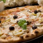 Making an artisan Artichoke Pizza at home has never been easier with this recipe featuring artichoke hearts, sliced mushrooms, and fresh olives.