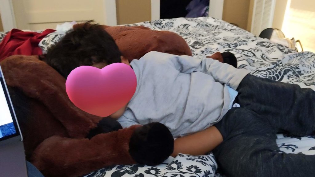 an emoji heart obscures the face of a young boy laying on a stuffed horse with both hands stuffed in his pockets.