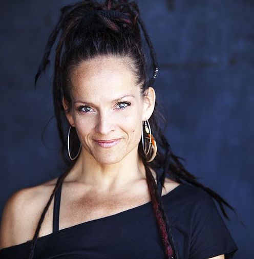 Woman with dreadlocks and hoop earrings, smiling against a dark background.